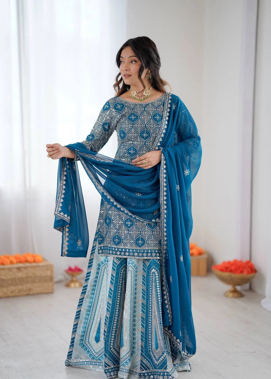 Woman in a blue and white traditional outfit with a matching dupatta, standing against a white curtain background.