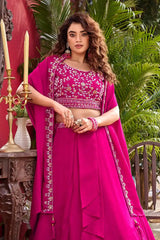 Woman in a bright pink traditional outfit with intricate designs, standing outdoors.