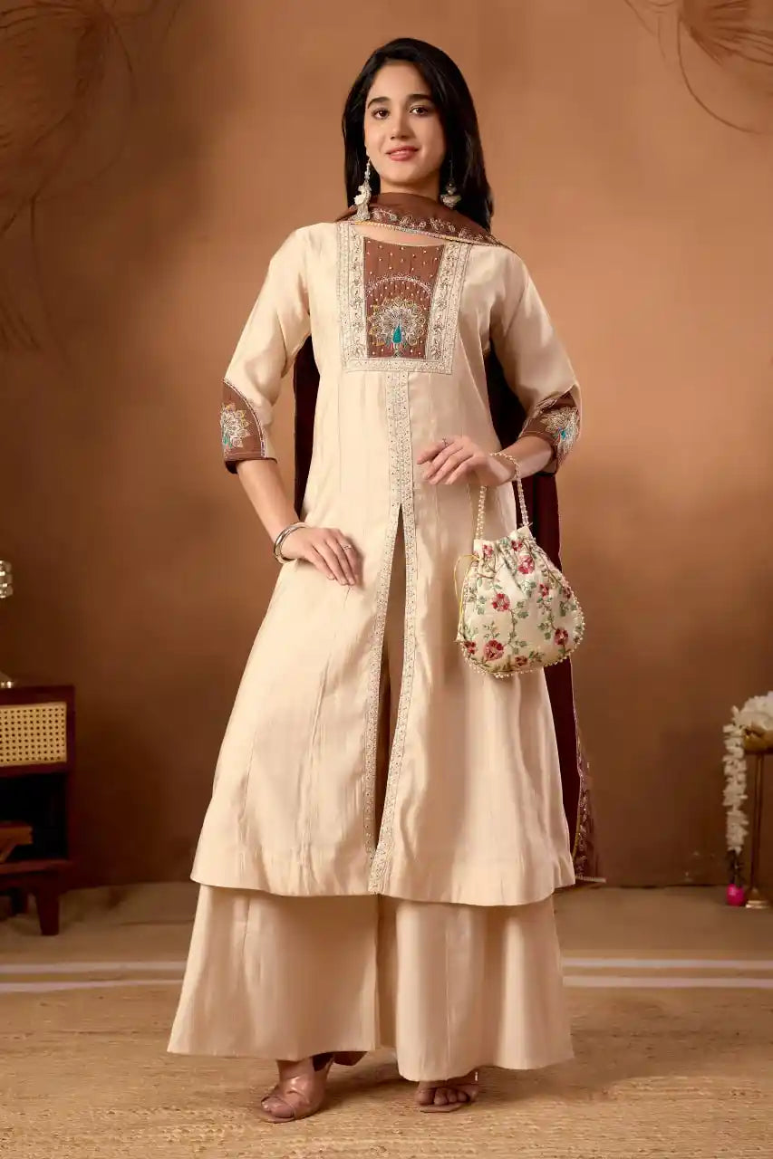 Woman wearing a beige traditional outfit with intricate patterns, holding a floral handbag against a brown background.