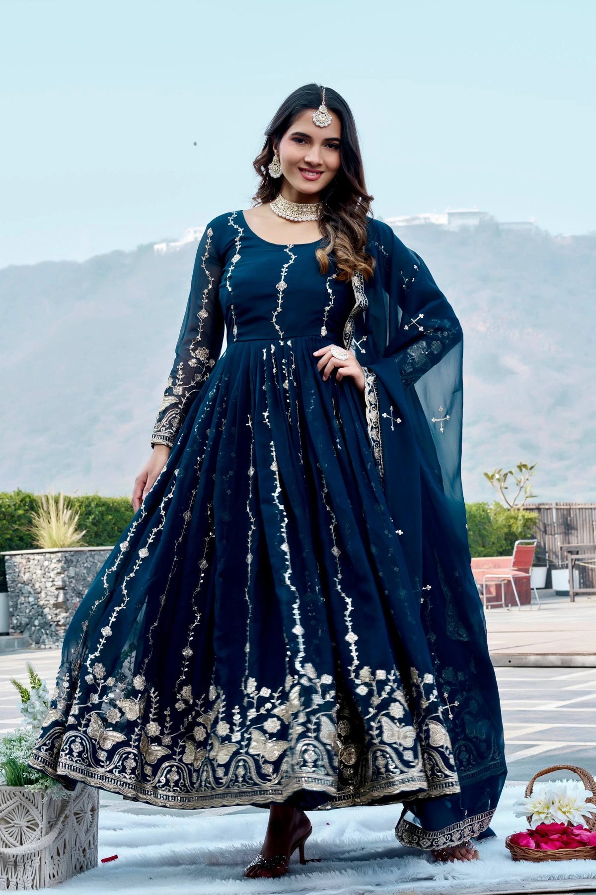 Woman in a dark blue embroidered dress standing outdoors with mountains in the background