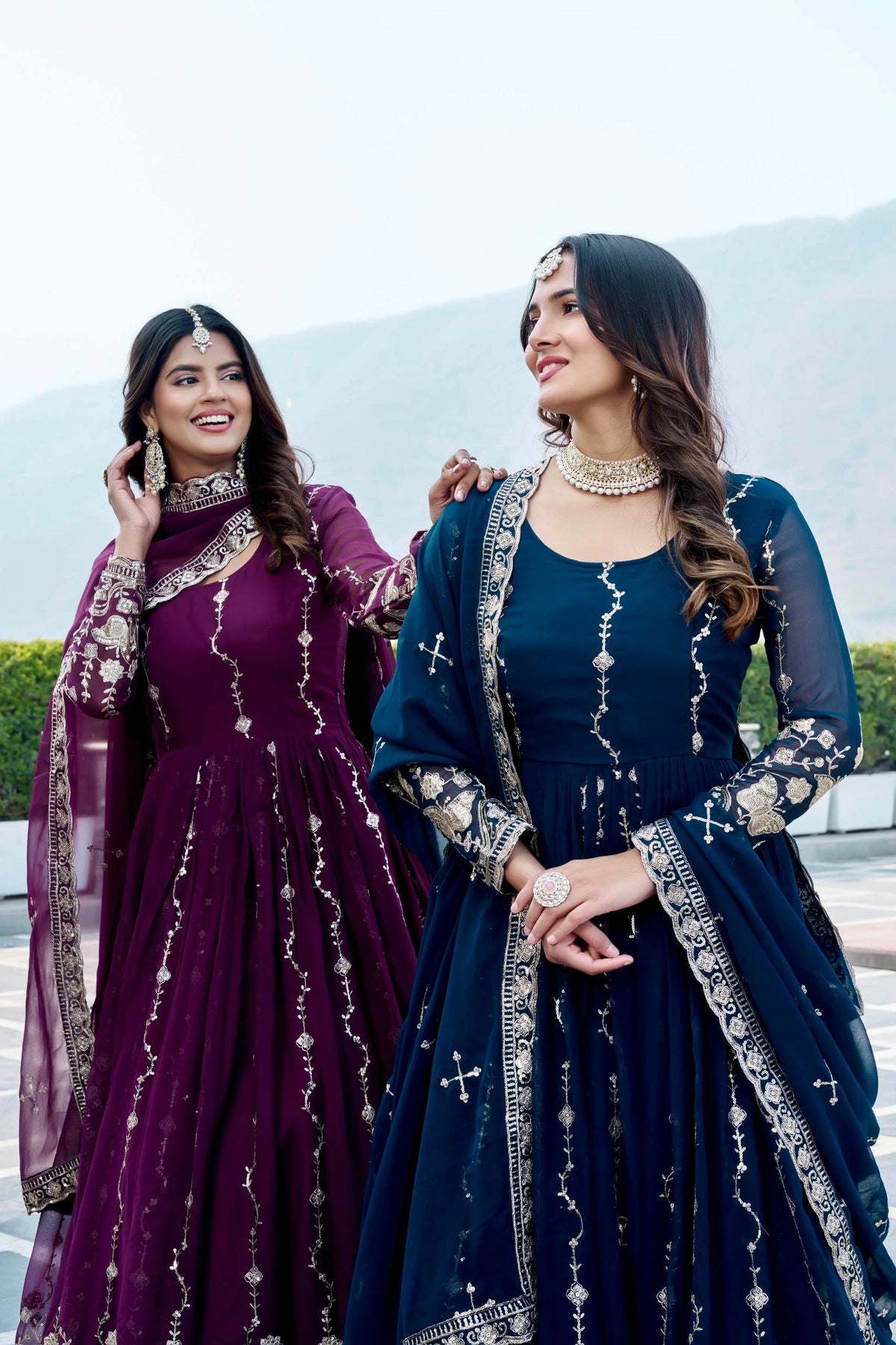 Two women in traditional outfits with embroidered designs outdoors.
