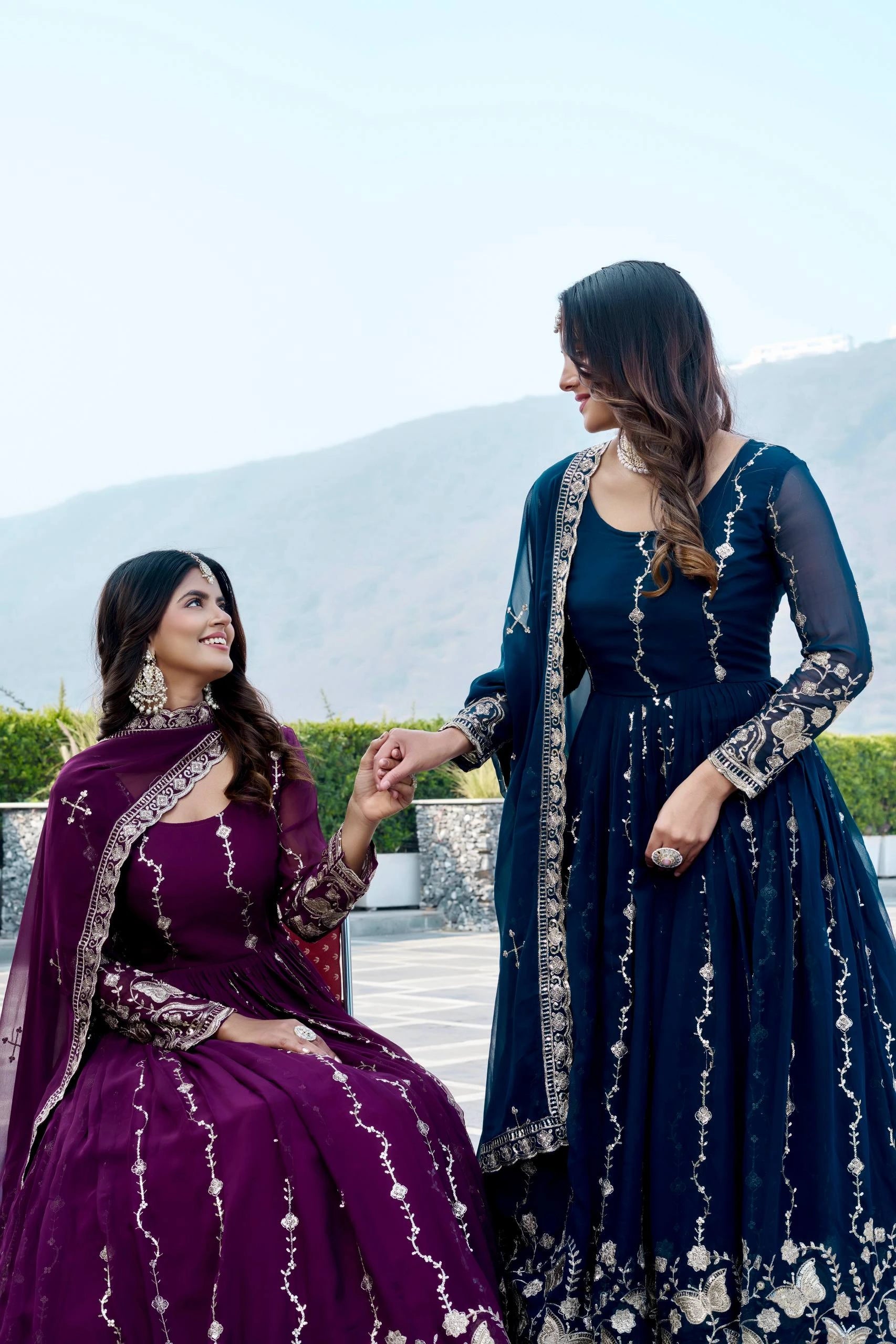 Two women in traditional outfits sitting outdoors with a mountainous background