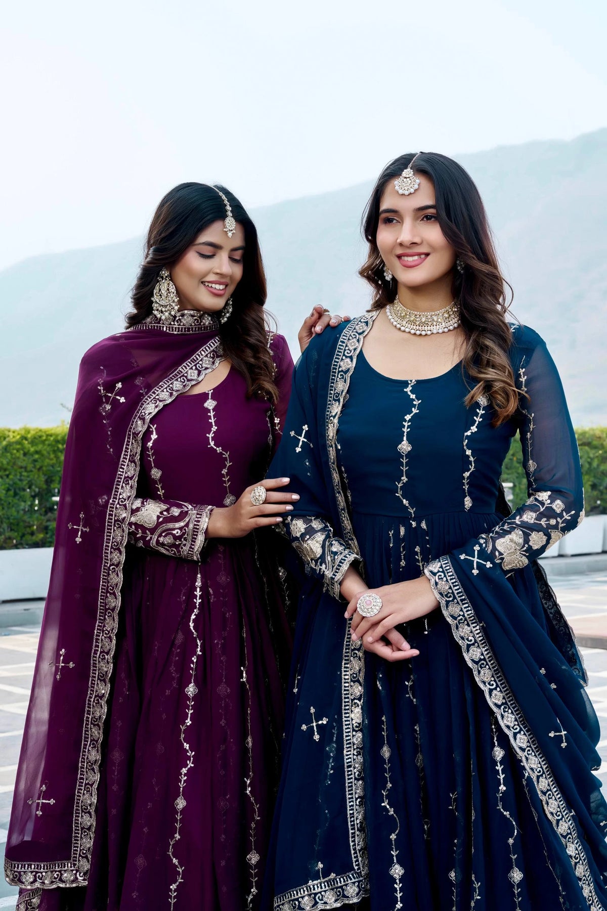 Two women in traditional attire standing outdoors with a scenic background.