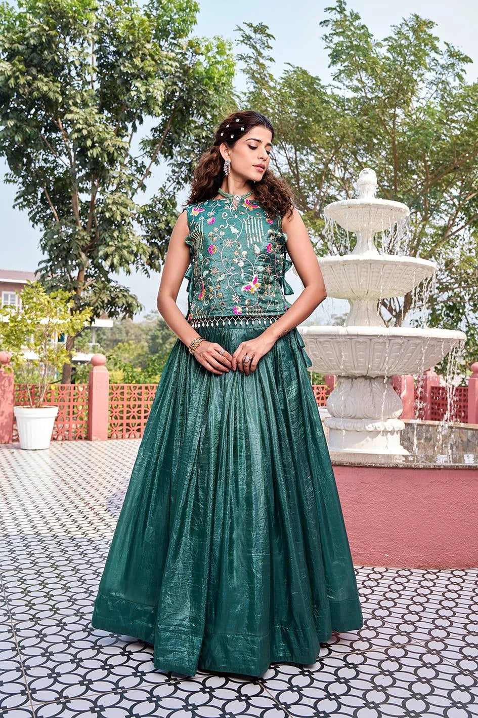 Woman in a green traditional outfit standing in front of a fountain with trees in the background