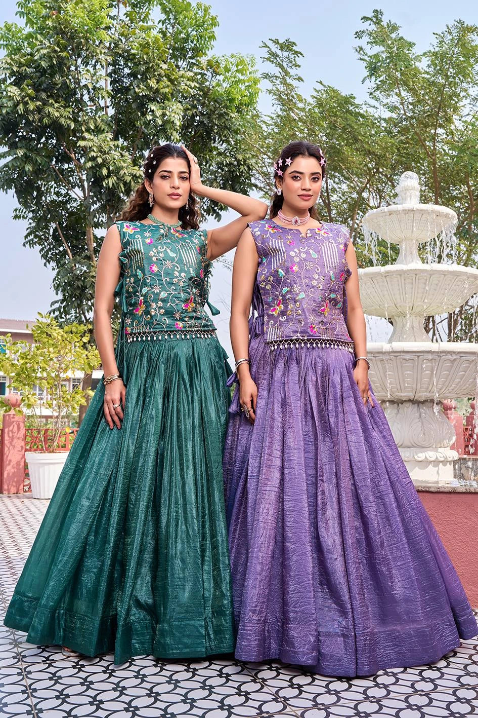 Two women in green and purple traditional dresses standing in front of a fountain.