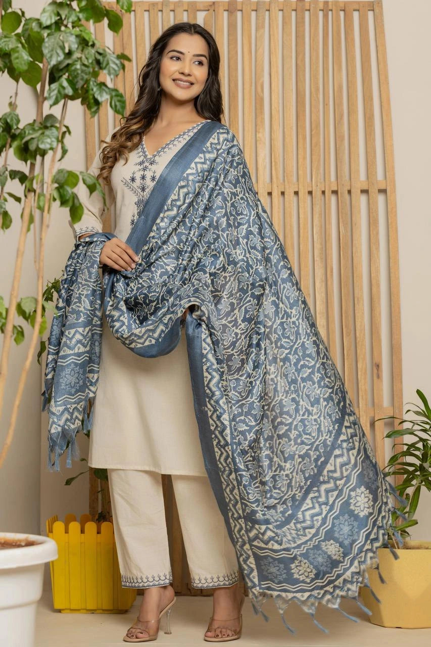 Woman wearing a blue patterned shawl over a white outfit in a home setting with plants.