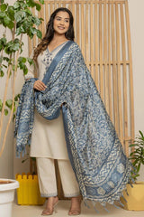 Woman wearing a blue patterned shawl over a white outfit in a home setting with plants.