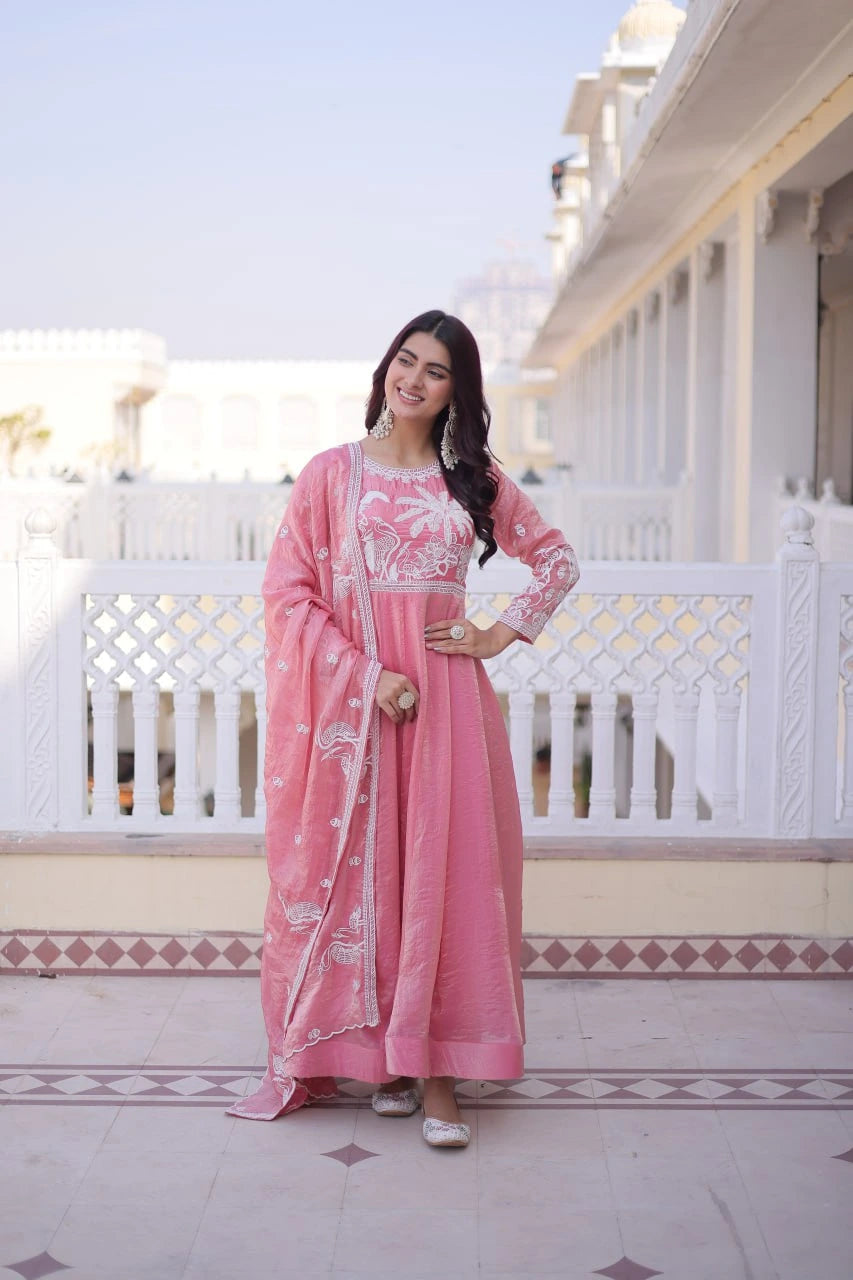 Woman in a pink traditional outfit standing on a balcony with white railing and architectural details.