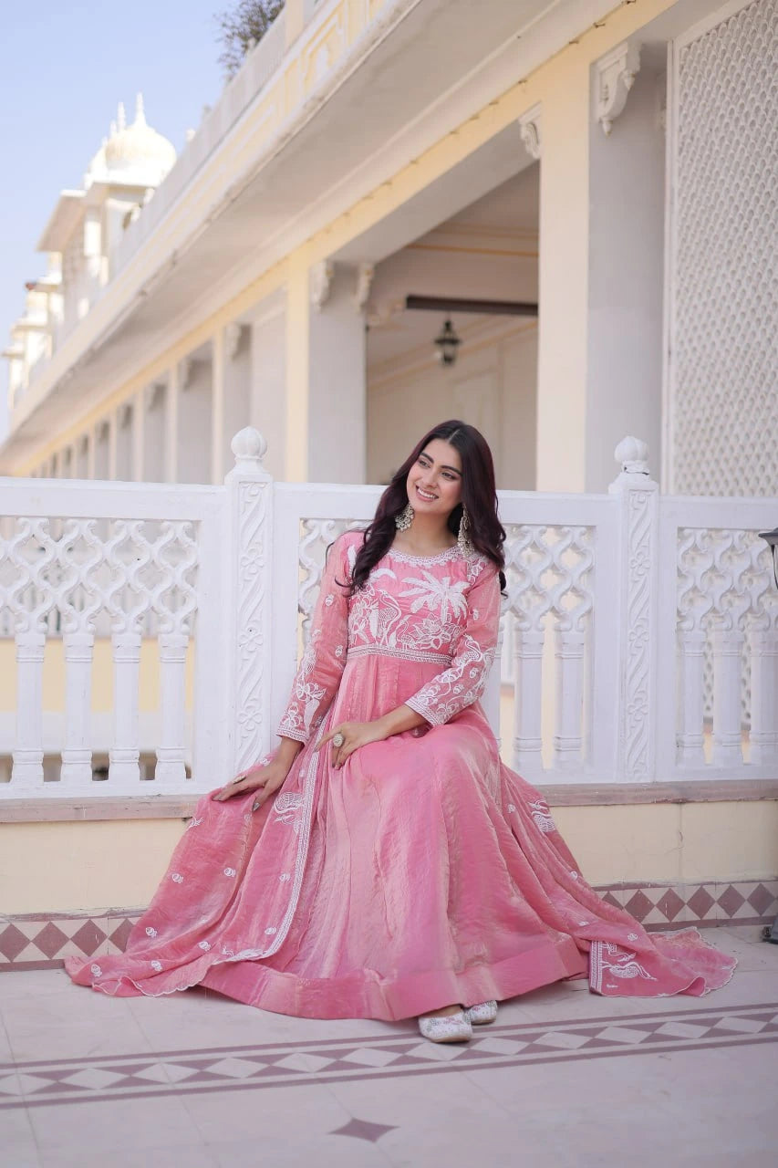 Woman in a pink traditional outfit standing on a balcony with white railings and architectural details.