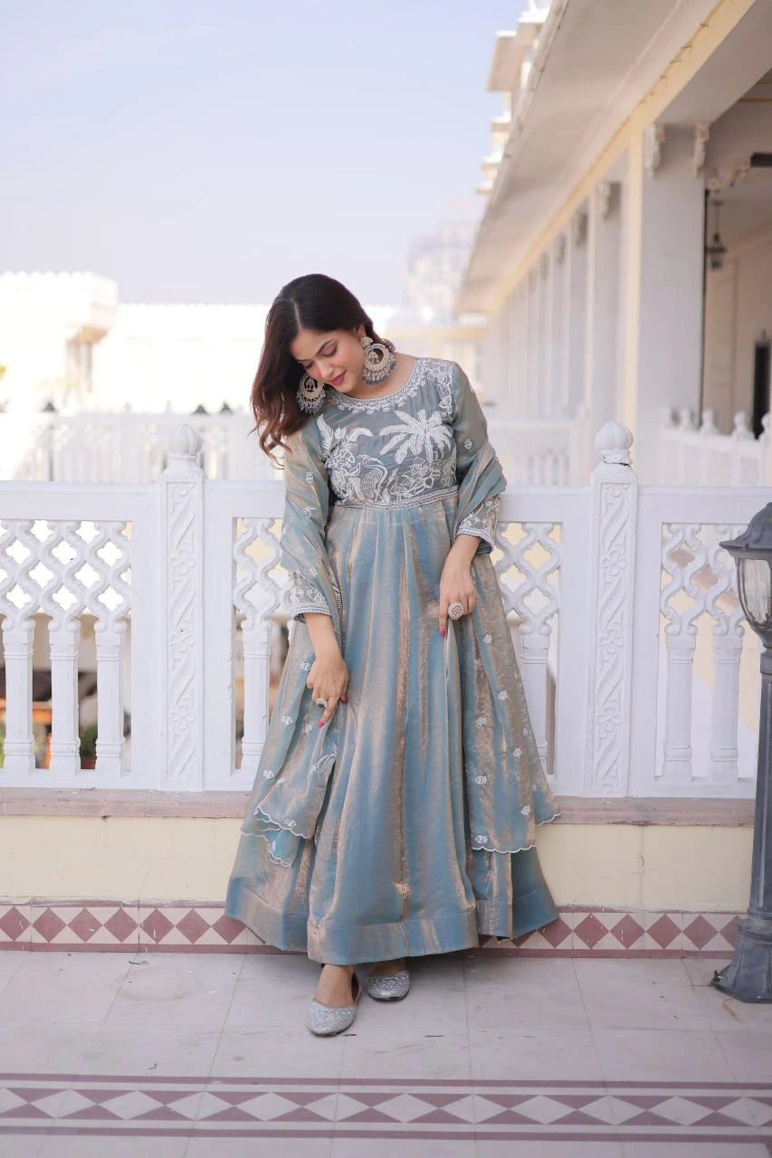 Woman in a long, light blue dress with floral patterns standing on a balcony.