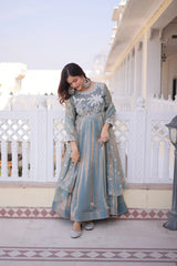 Woman in a long, light blue dress with floral patterns standing on a balcony.