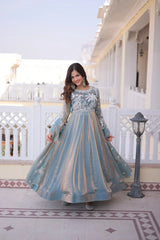 Woman in a long, light blue and white patterned dress standing on a balcony.