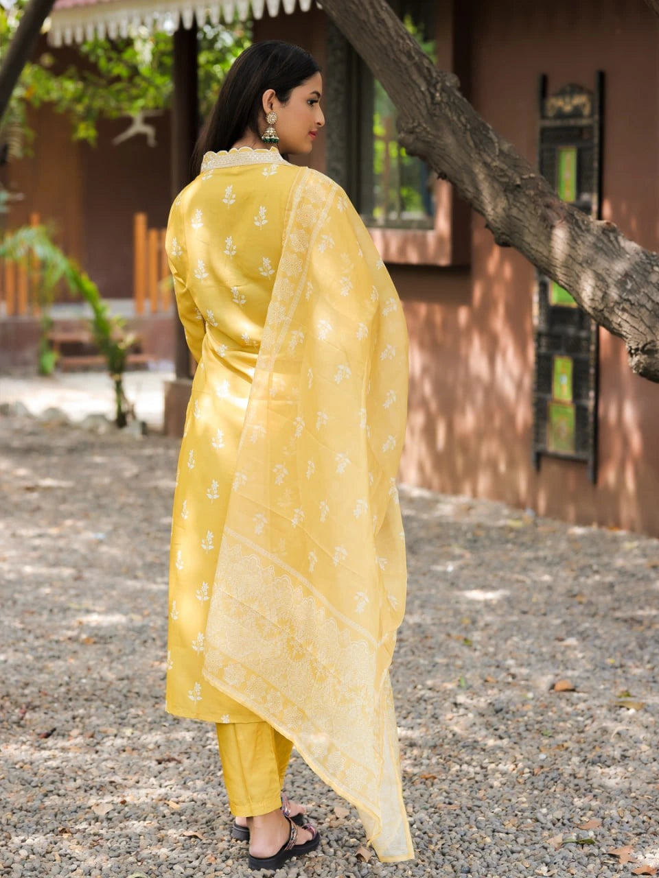 Woman in a yellow traditional outfit standing outdoors near a tree