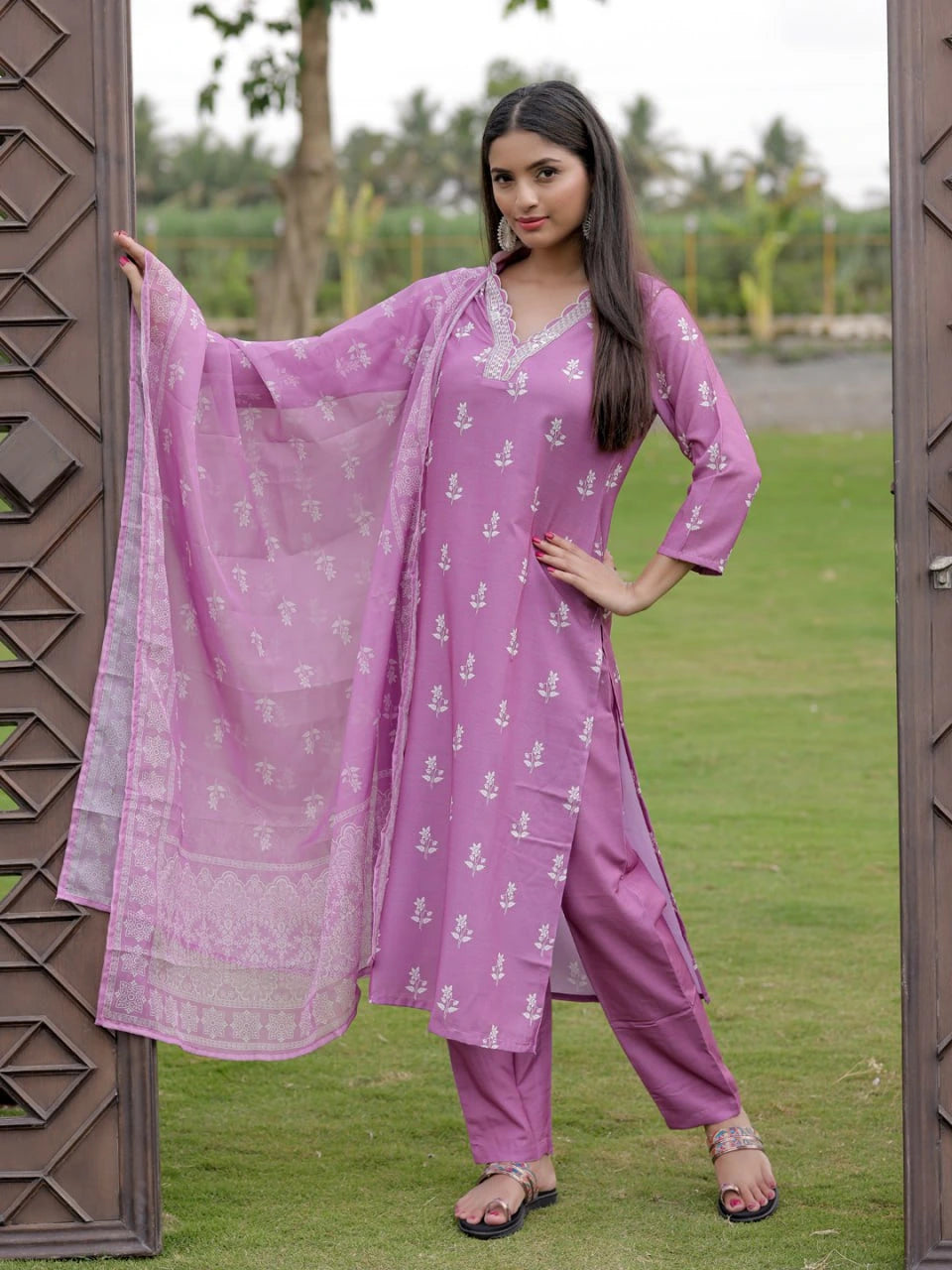 Woman in a pink traditional outfit standing outdoors with greenery in the background