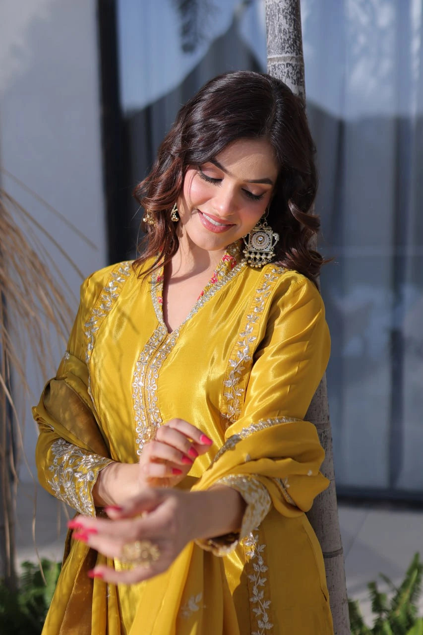 Woman in a yellow traditional outfit with intricate designs, standing outdoors.