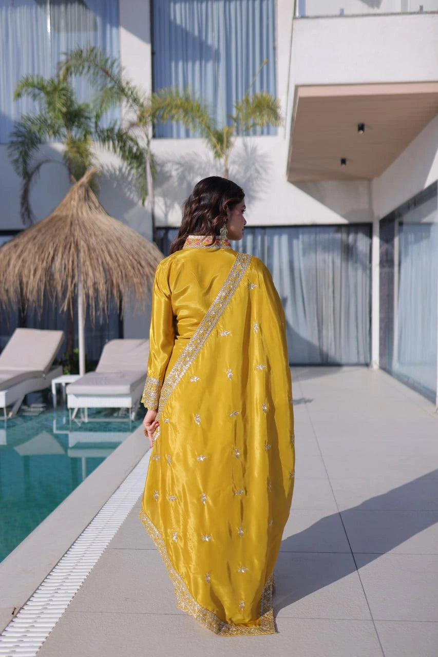 Woman in a yellow saree standing by a poolside with modern architecture in the background
