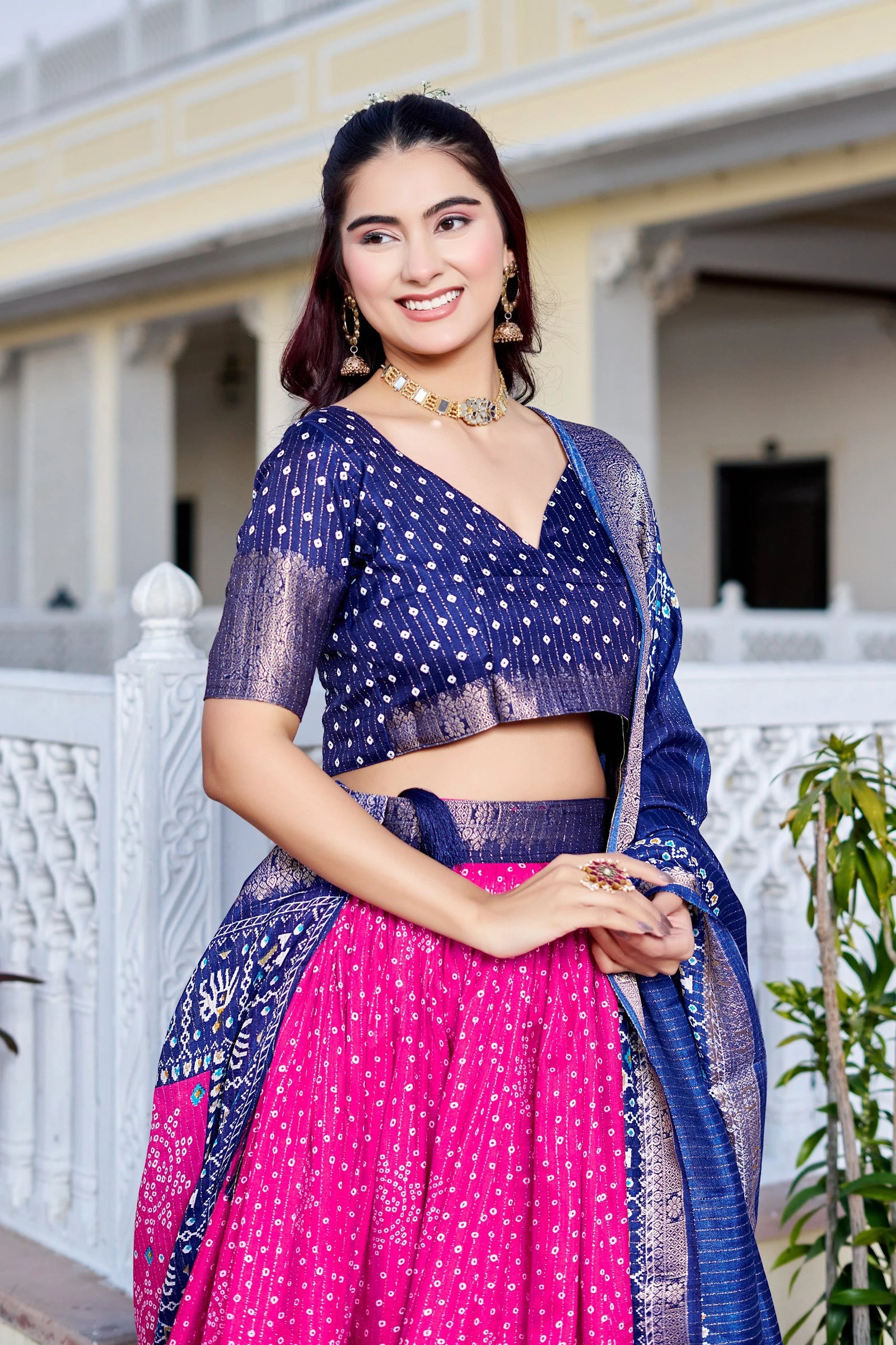 Woman wearing a traditional outfit with a blue blouse and pink saree in front of a white building.