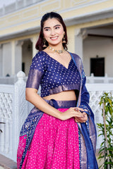 Woman wearing a traditional outfit with a blue blouse and pink saree in front of a white building.