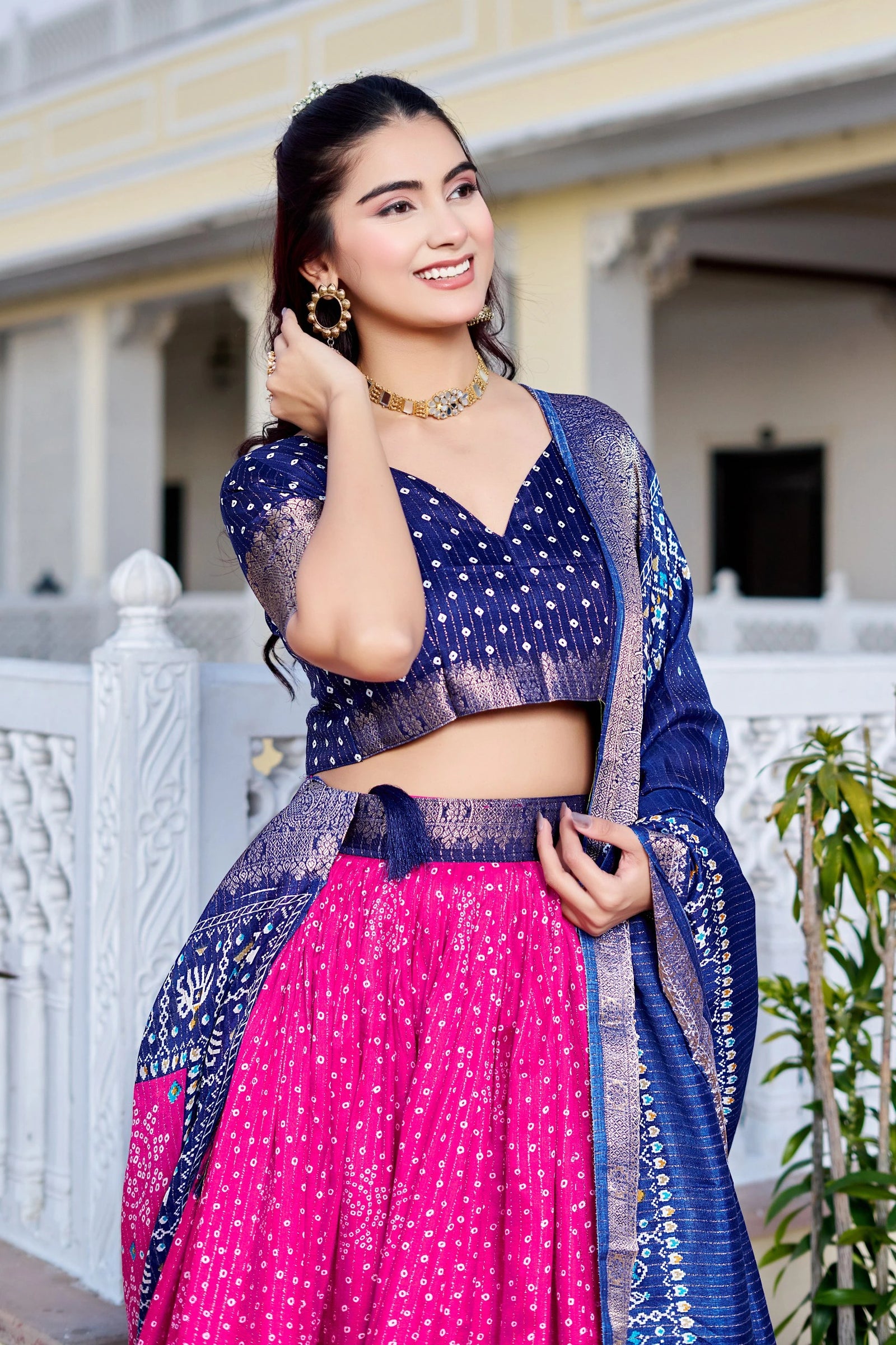 Woman in a traditional outfit with a blue and pink saree standing outdoors.