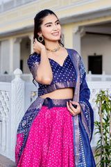 Woman in a traditional outfit with a blue and pink saree standing outdoors.