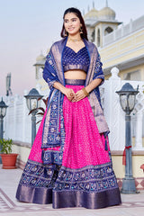 Woman in a traditional pink and blue outfit standing outdoors with architectural elements in the background