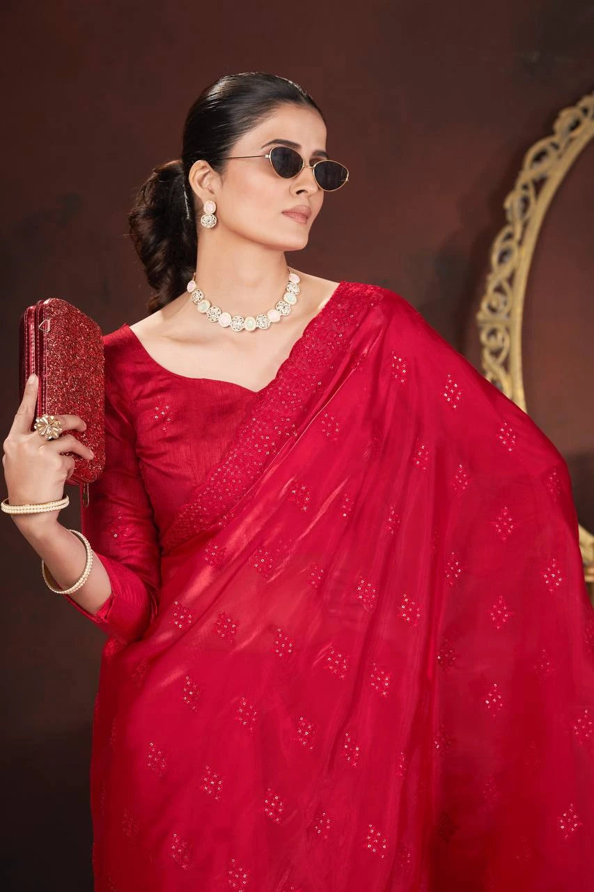 Woman in a red saree holding a clutch against a dark background