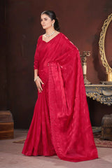 Woman in a red saree standing in a room with decorative elements.