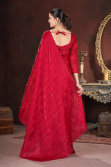 Woman in a red saree standing in a room with a decorative mirror and furniture.