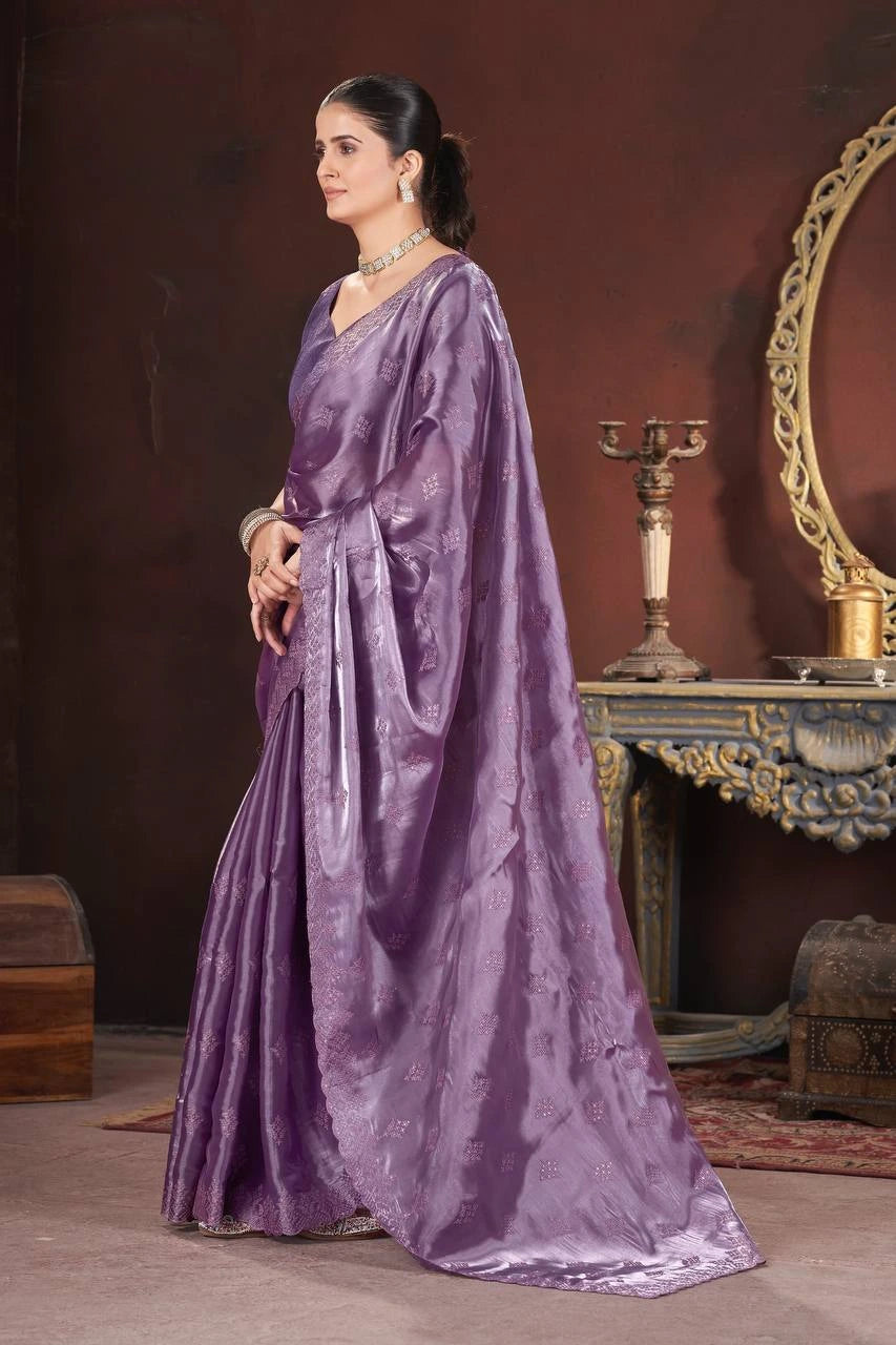 Woman in a purple saree standing in a room with a mirror and decorative items.