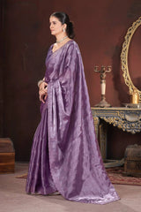 Woman in a purple saree standing in a room with a mirror and decorative items.