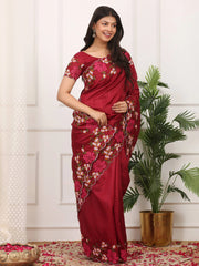 Woman wearing a red saree with floral patterns in a decorated room.