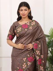 Woman wearing a brown saree with floral embroidery against a white background