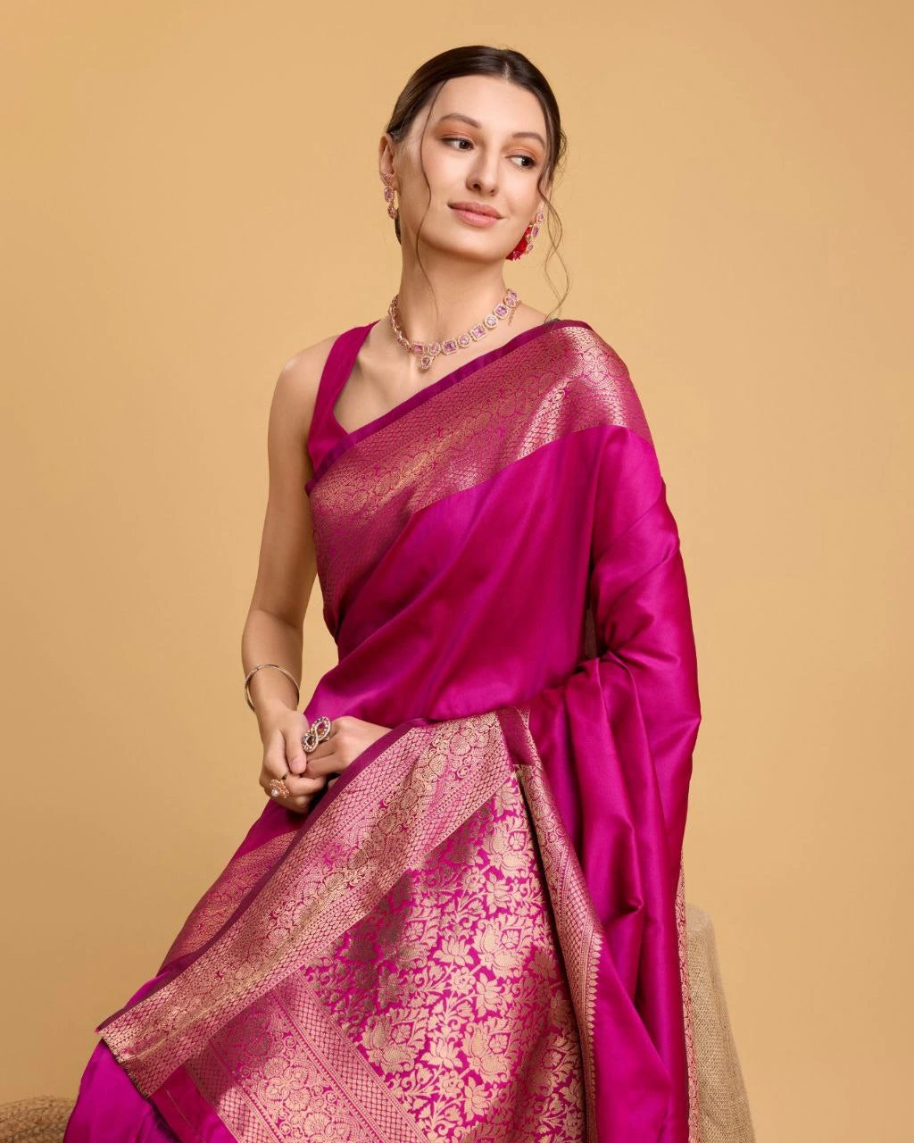 Woman wearing a pink saree with a gold border on a beige background