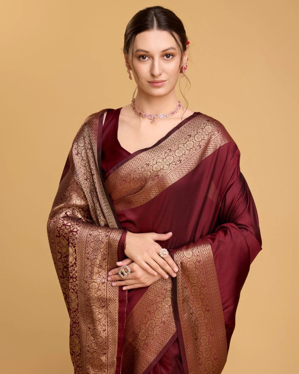 Woman wearing a maroon saree with gold patterns on a beige background