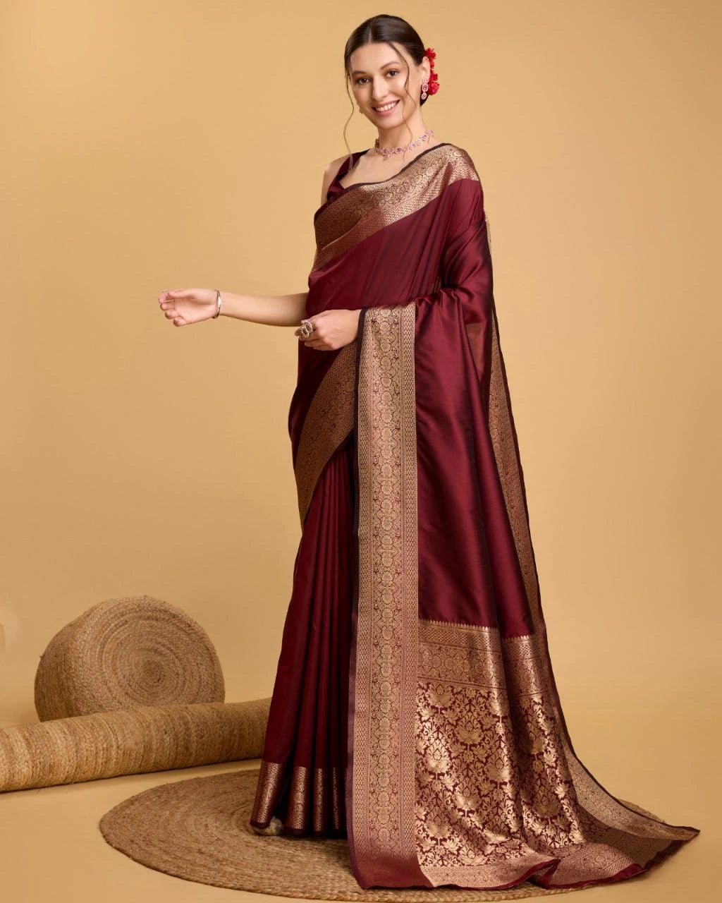 Woman wearing a maroon saree with gold border on a beige background