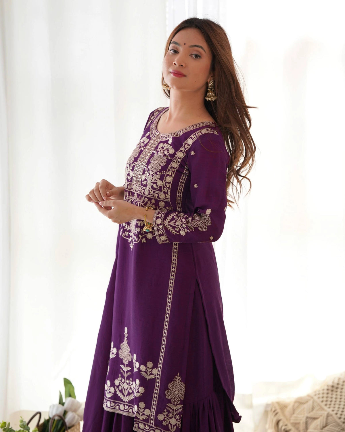 Woman wearing a purple embroidered dress against a white curtain background