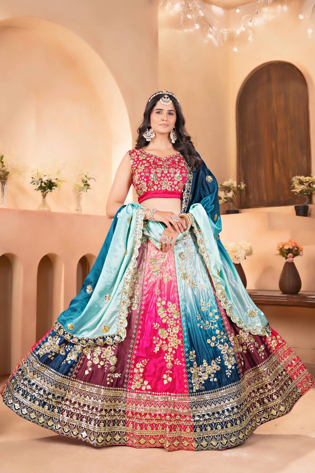 Woman in a traditional embroidered lehenga with a pink blouse in an elegant indoor setting.