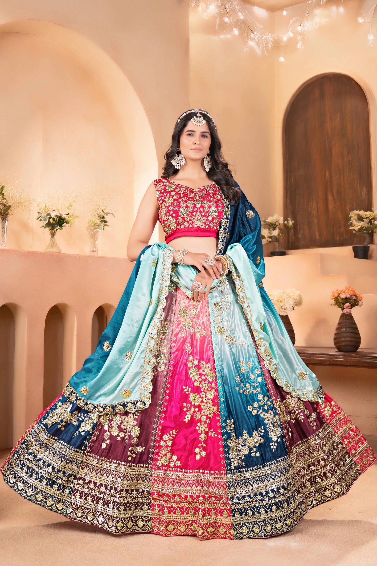 Woman in a traditional embroidered lehenga with a pink blouse in an elegant indoor setting.