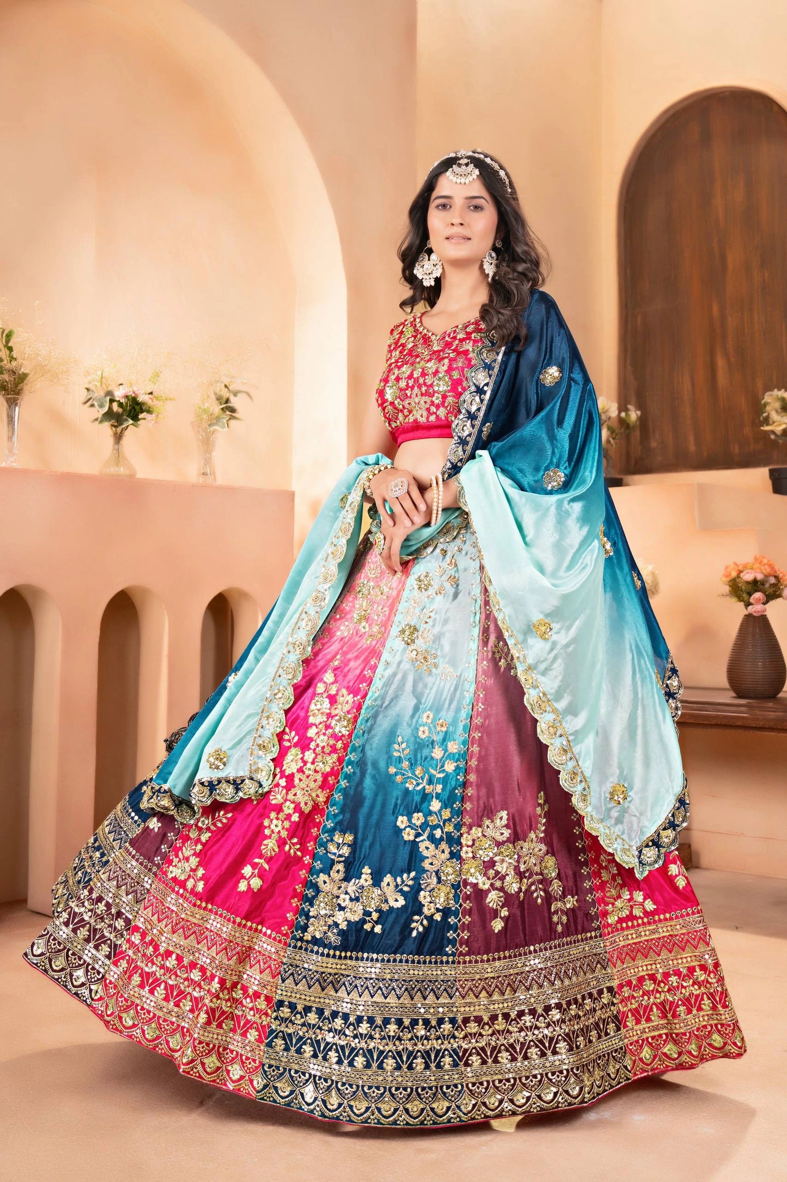 Woman in a traditional embroidered lehenga with pink and blue colors in an indoor setting.
