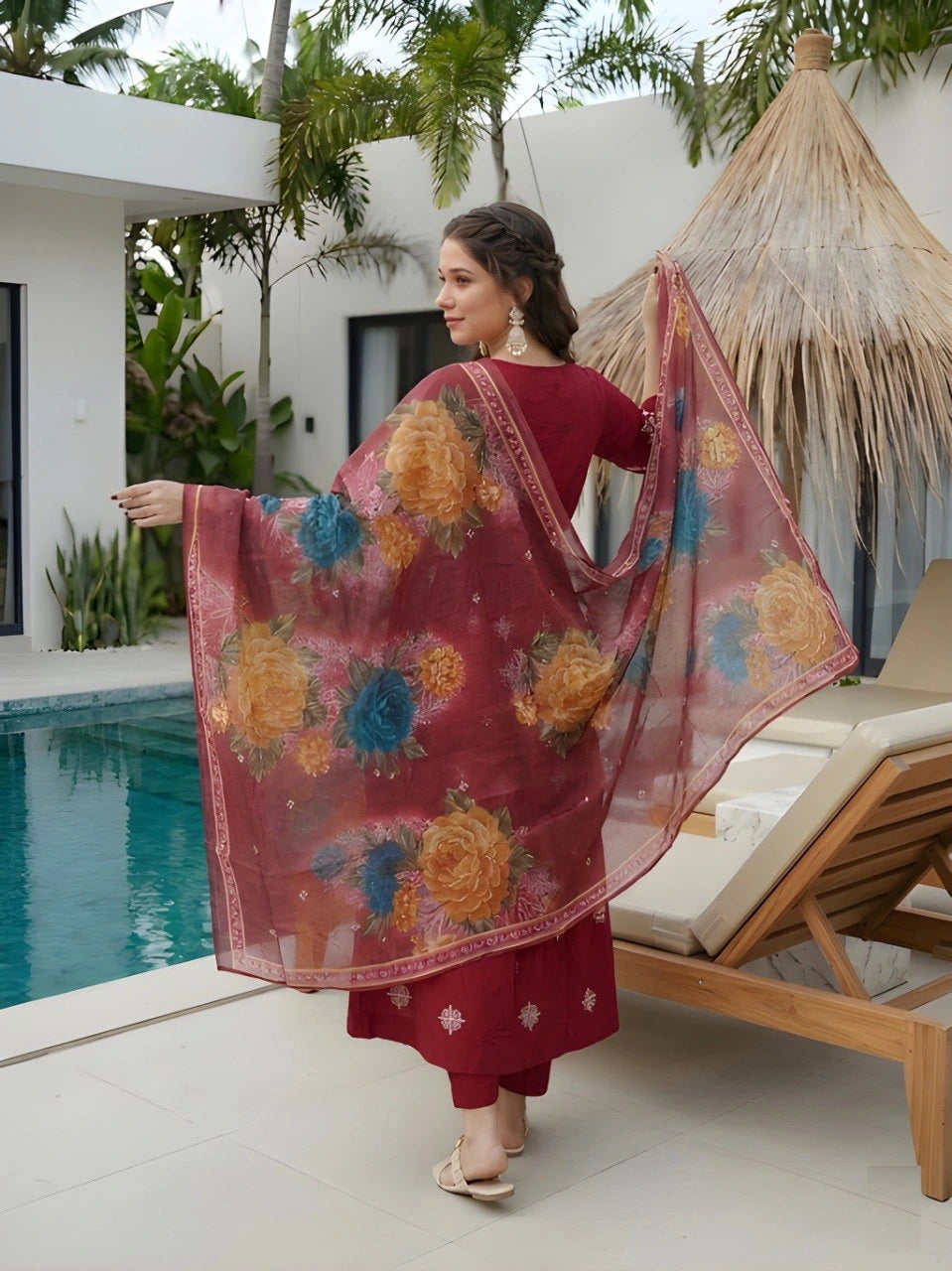 Woman in a red traditional outfit with a floral dupatta by a poolside.
