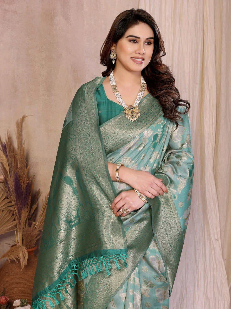 Woman wearing a green saree with a matching blouse against a beige curtain background