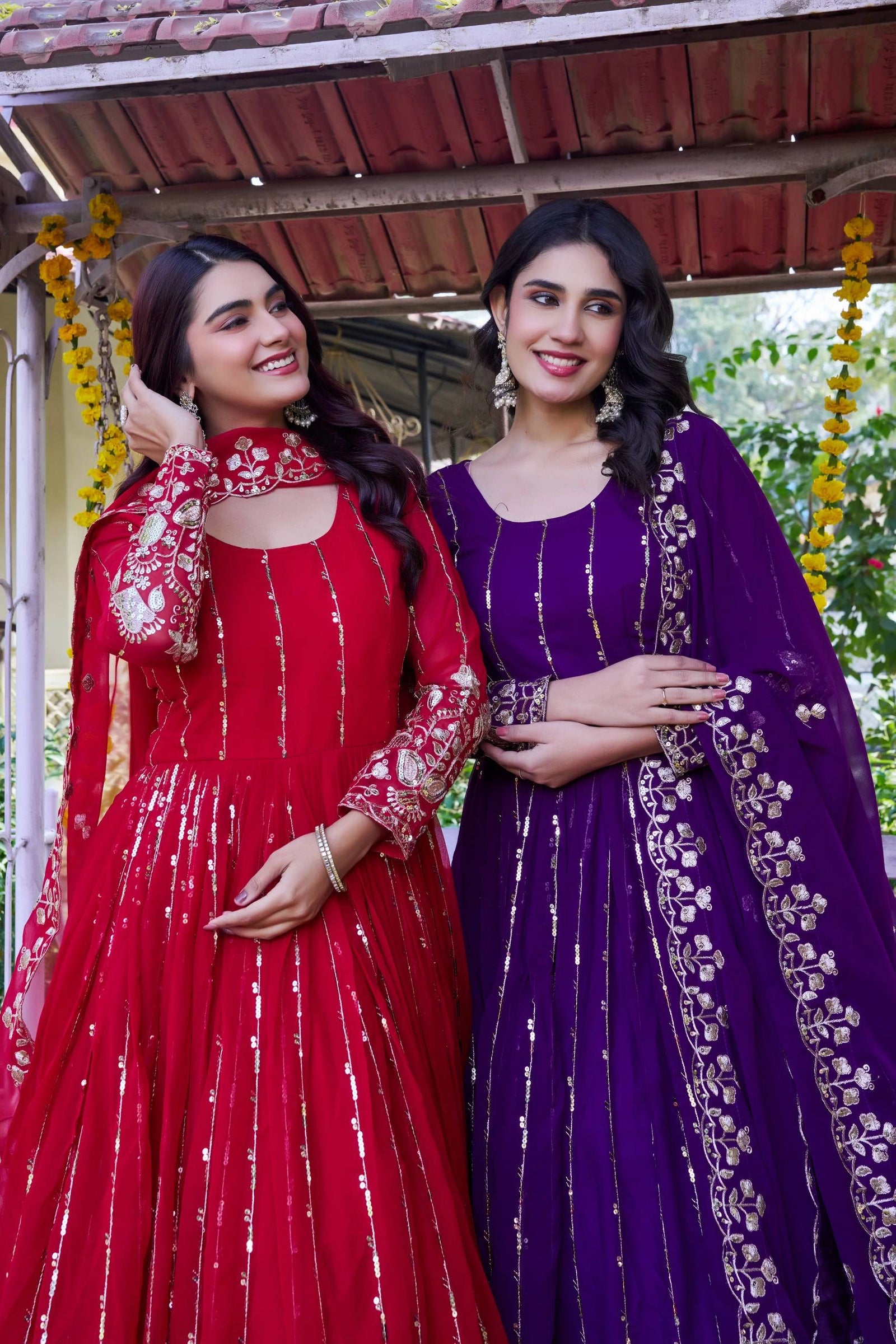 Two women in traditional red and purple dresses standing together outdoors.