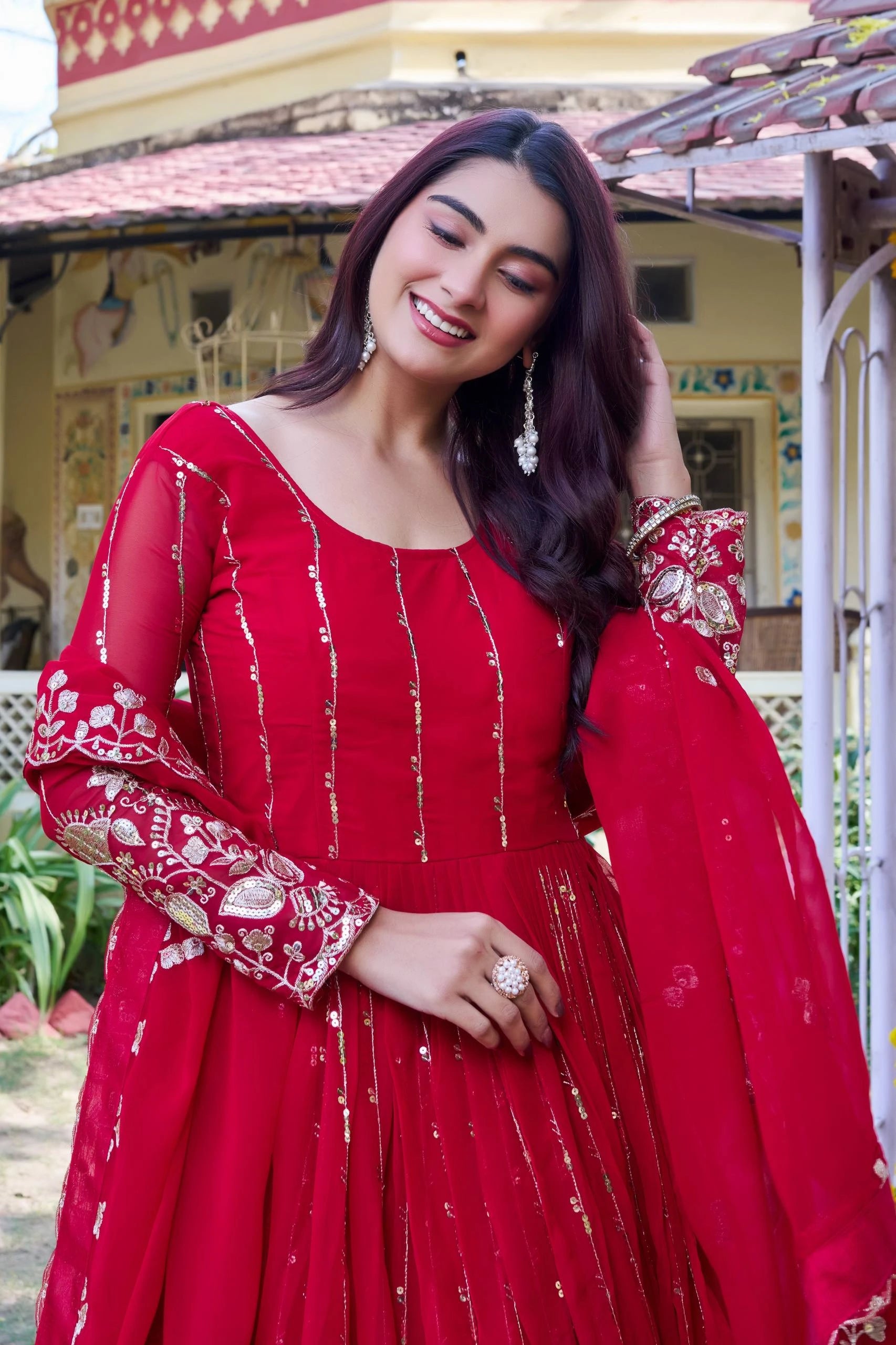 Woman in a red traditional outfit with white embroidery standing outdoors.