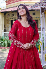 Woman in a red traditional outfit standing outdoors with a building and garden in the background