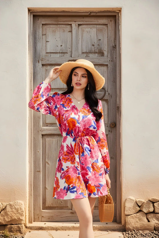 Woman in a colorful floral dress and straw hat standing in front of a wooden door.