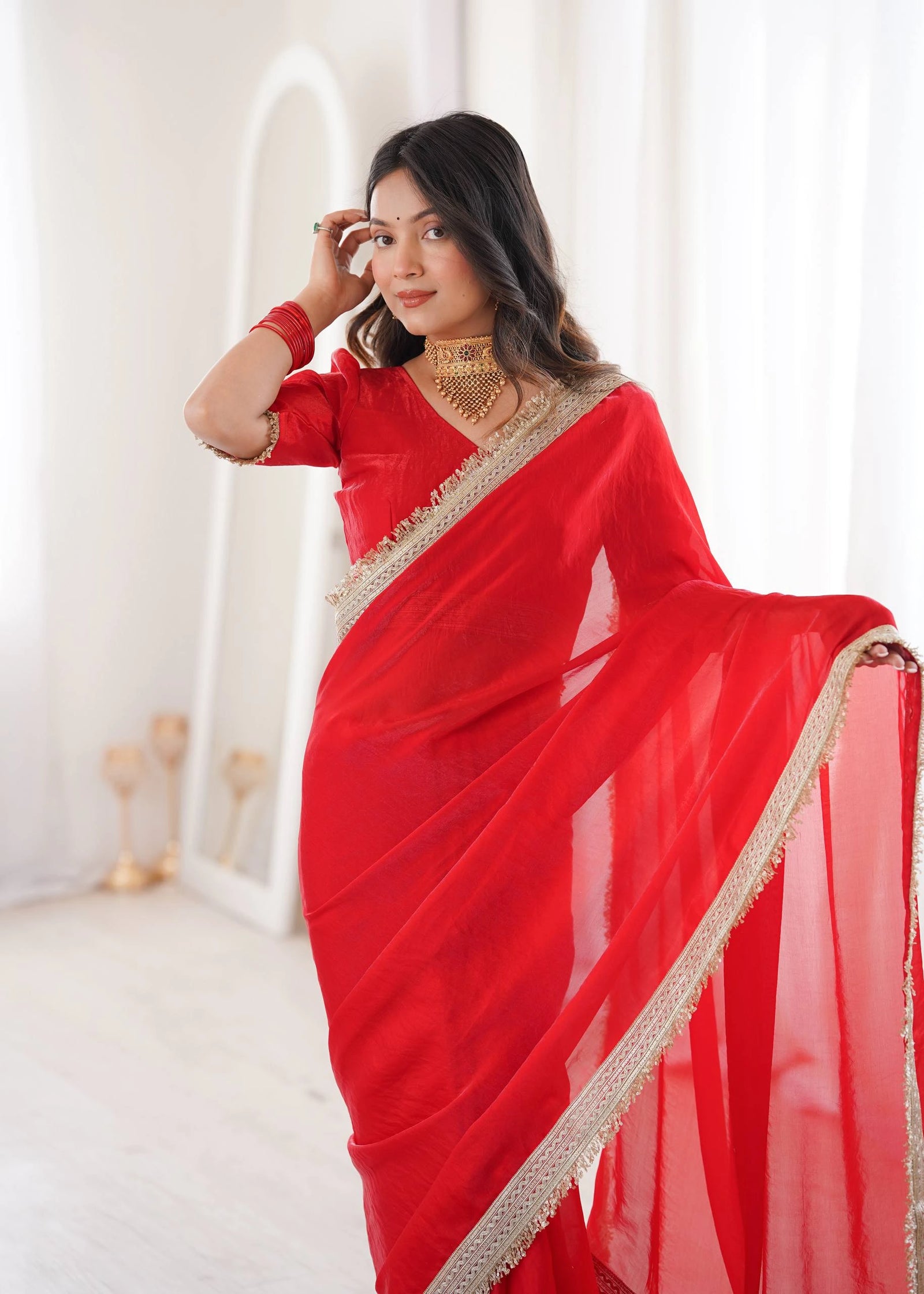 Woman wearing a red saree with gold border against a white background