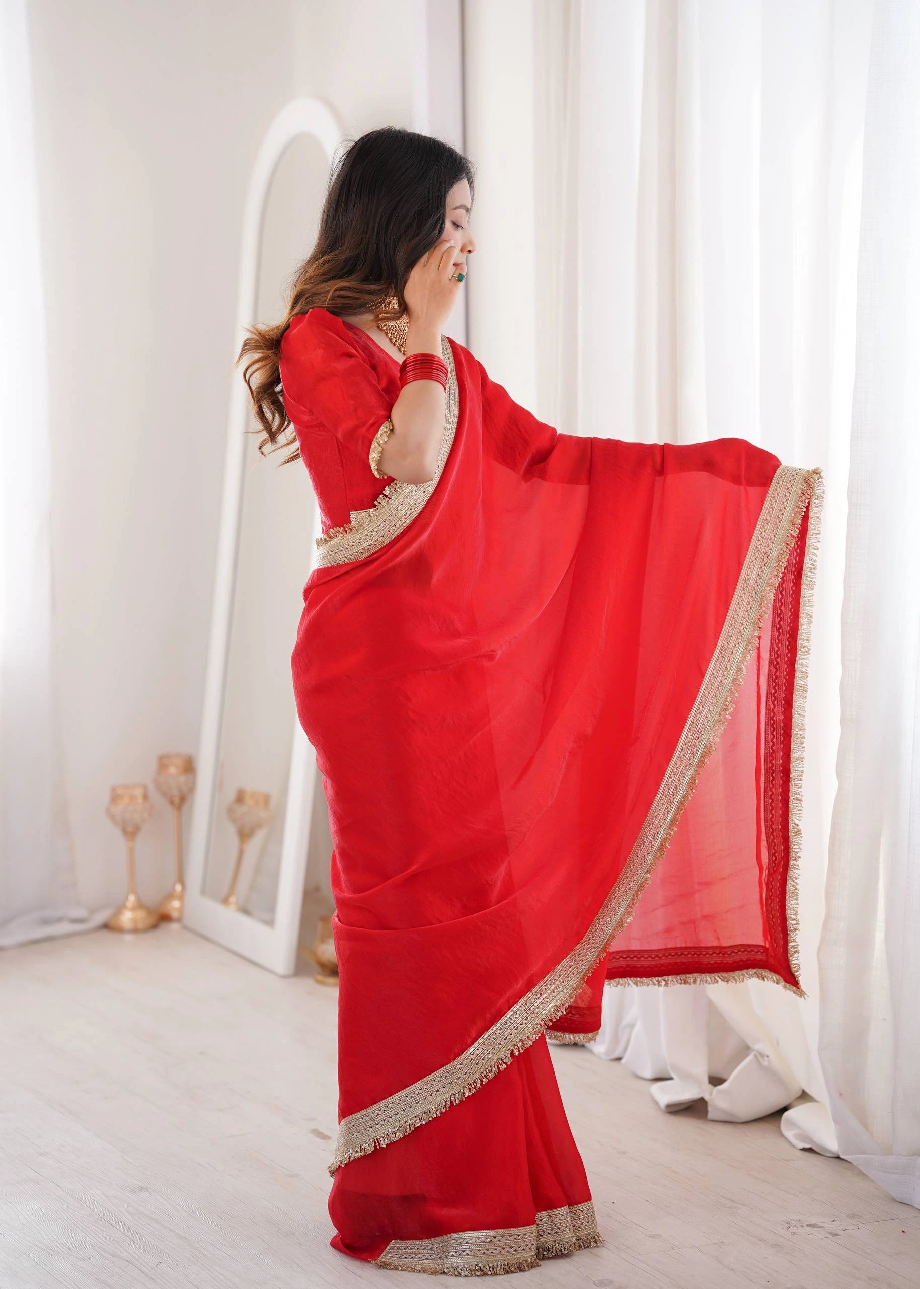 Woman wearing a red saree with gold border in a white room.