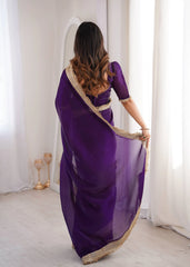 Woman wearing a purple saree with gold border in a room with white curtains.
