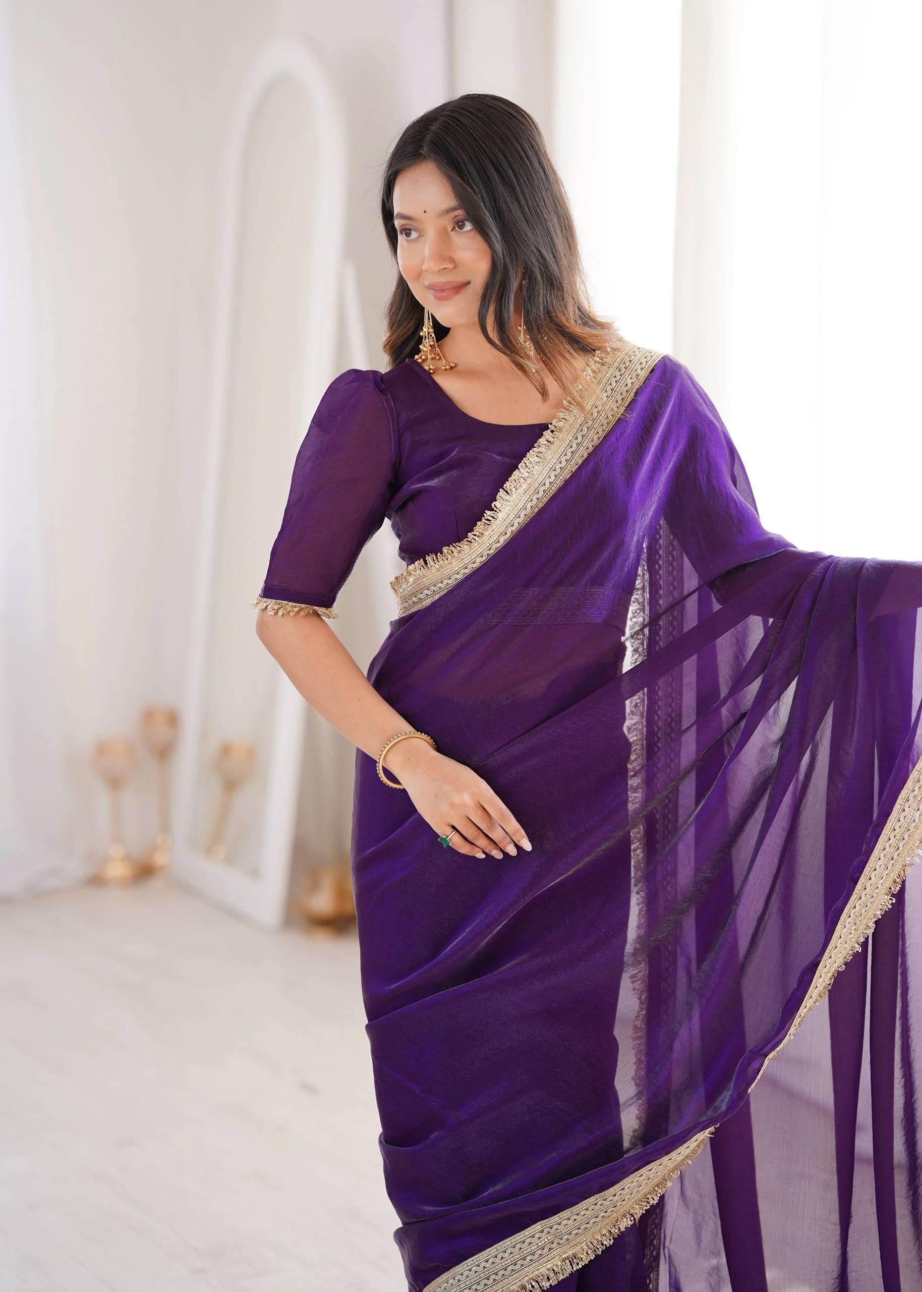 Woman wearing a purple saree with gold border in a white room