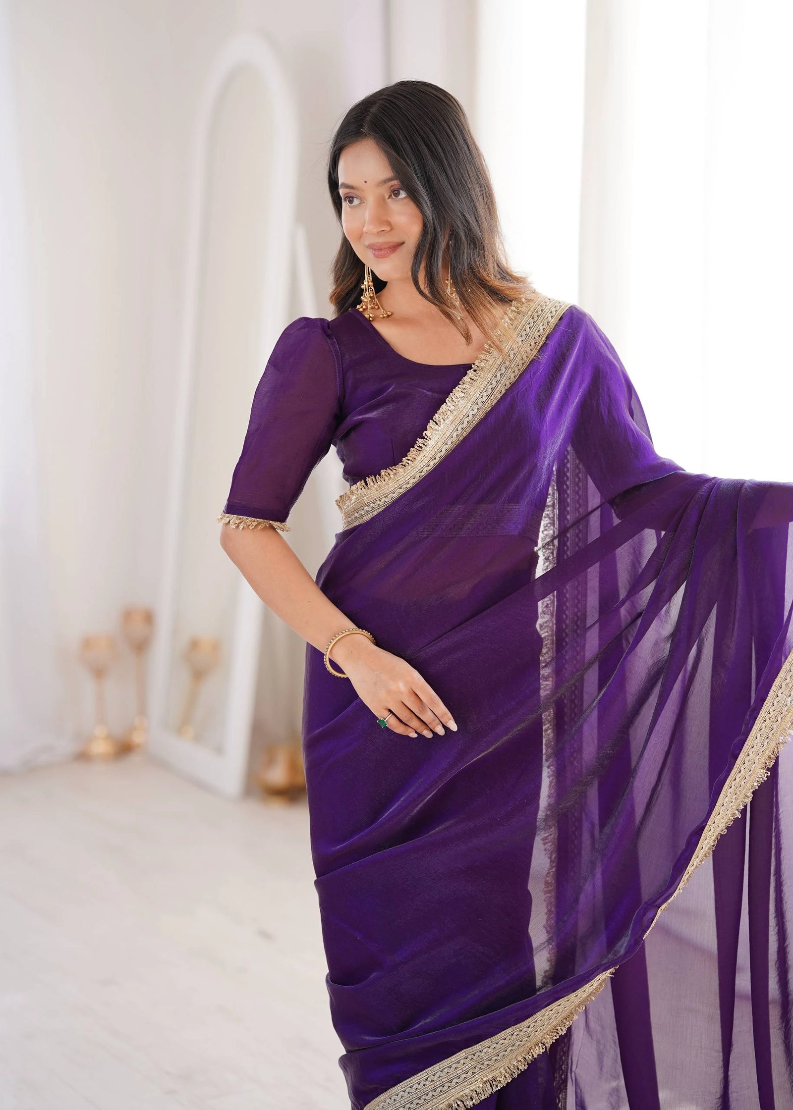 Woman wearing a purple saree with gold border in a white room